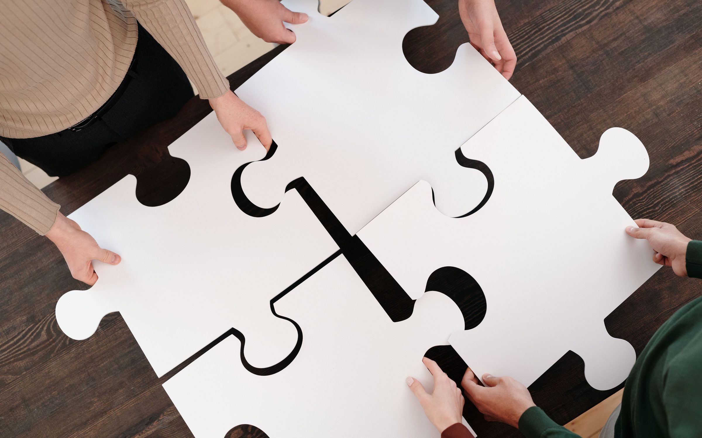 Hands fitting large puzzle pieces together on a table