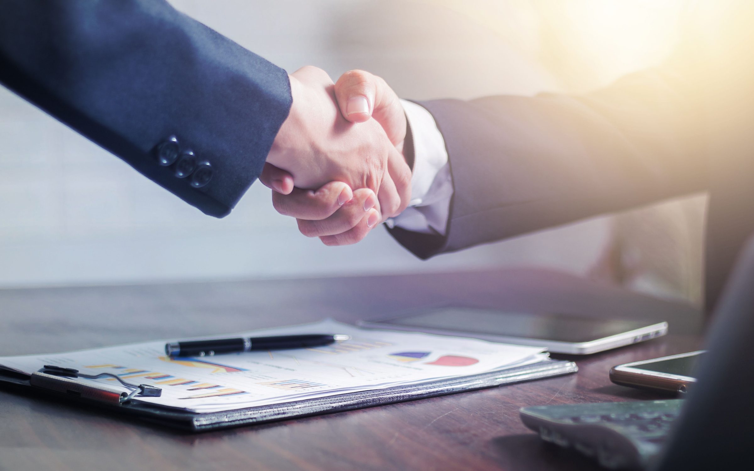 Two professionals shaking hands over signed documents